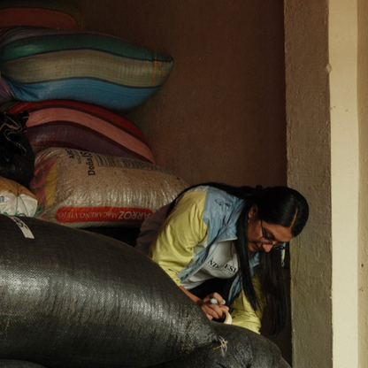 Person sitting on the floor with bags stacked around them in a dimly lit room.
