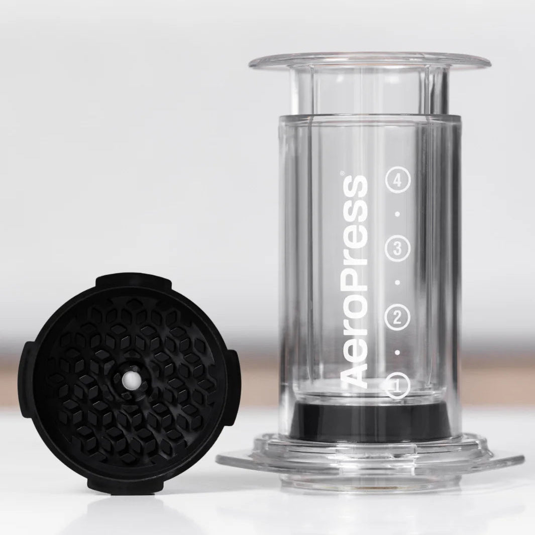 Clear AeroPress coffee maker with black rubber gasket on a white background