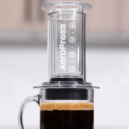 Aeropress coffee maker with a glass mug filled with coffee on a neutral background