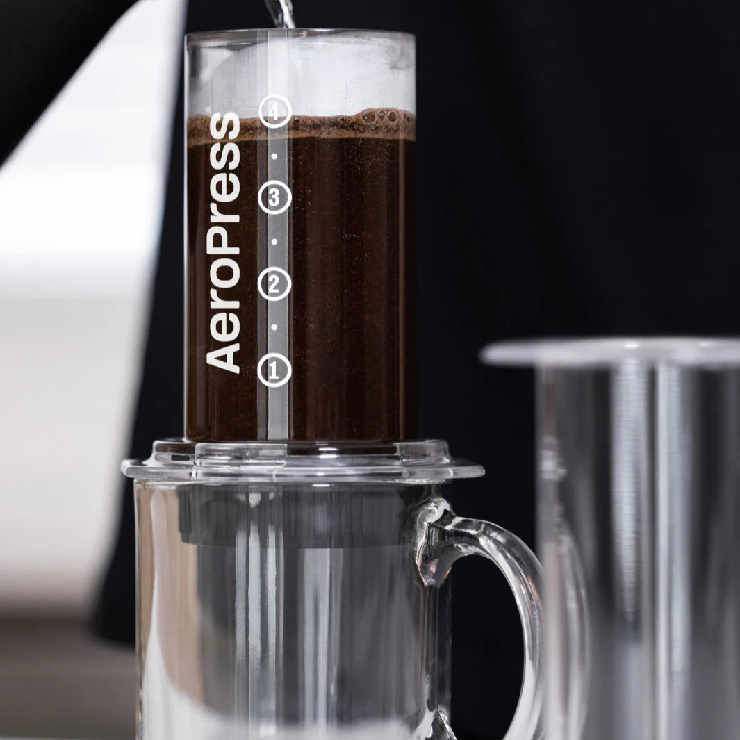 Aeropress coffee maker with coffee being poured into a clear mug.