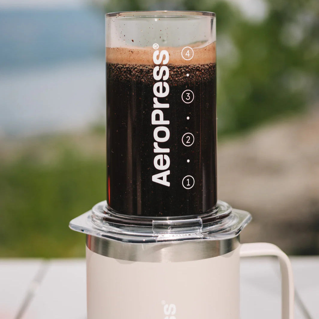 Aeropress coffee maker with coffee in a glass container outdoors.