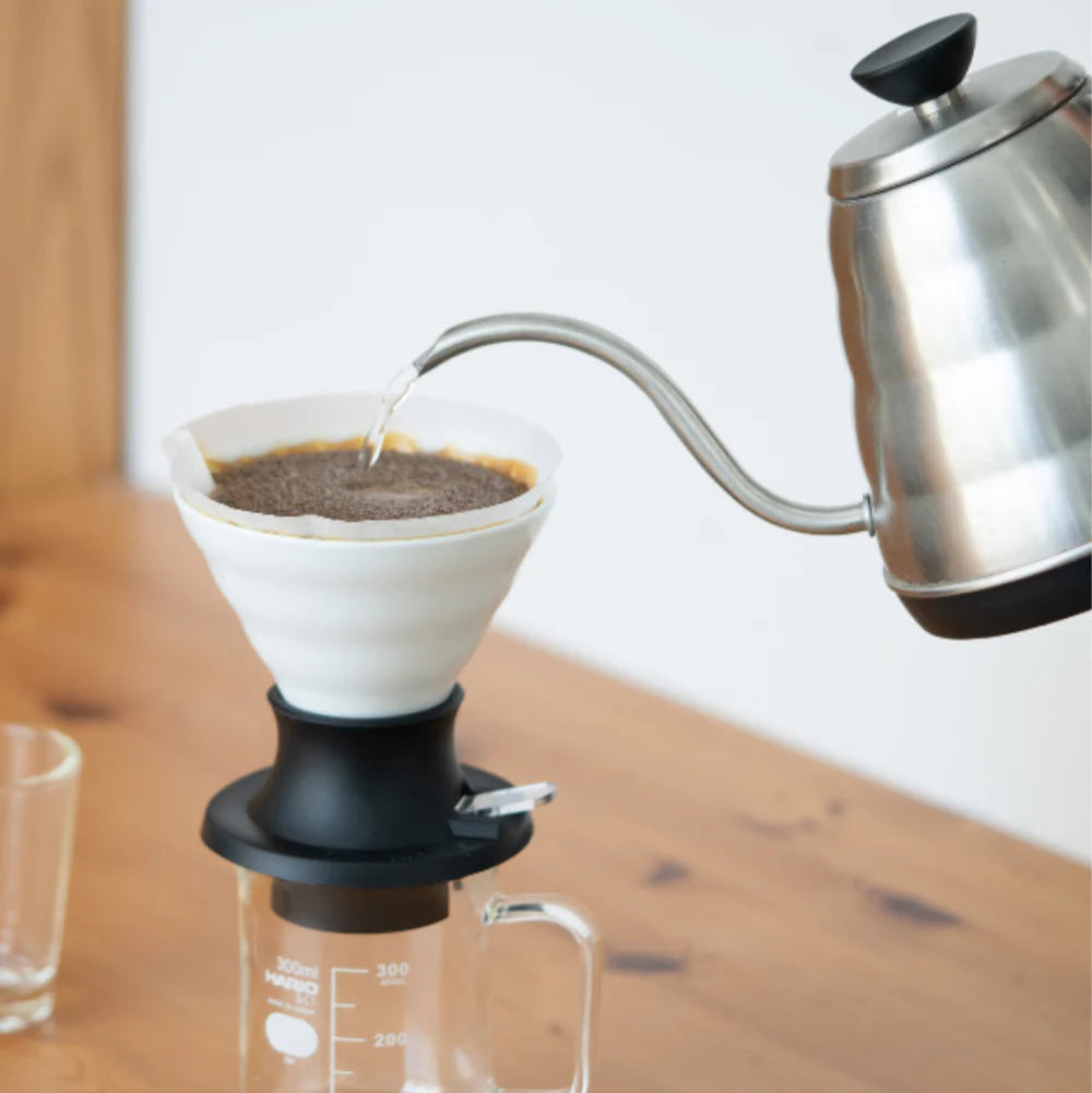 Coffee brewing setup with a kettle pouring water into a coffee filter on a wooden surface.